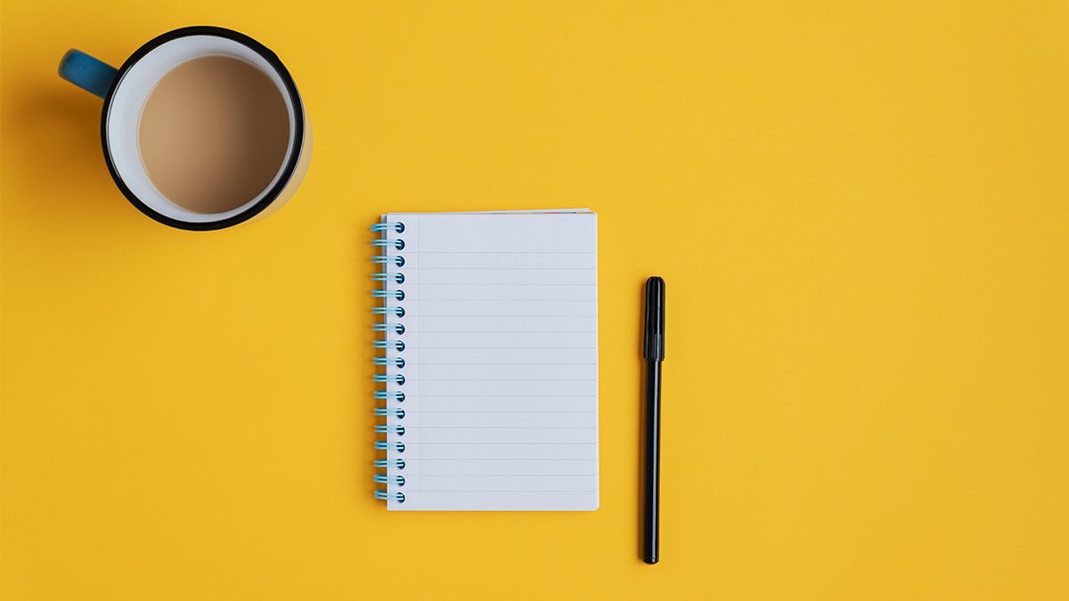 notepad and black pen with cup of coffee with cream on yellow background