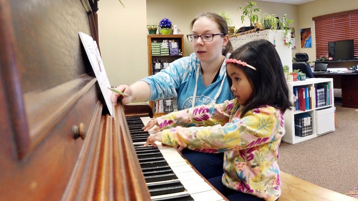 little girl practicing the piano next to her music teacher