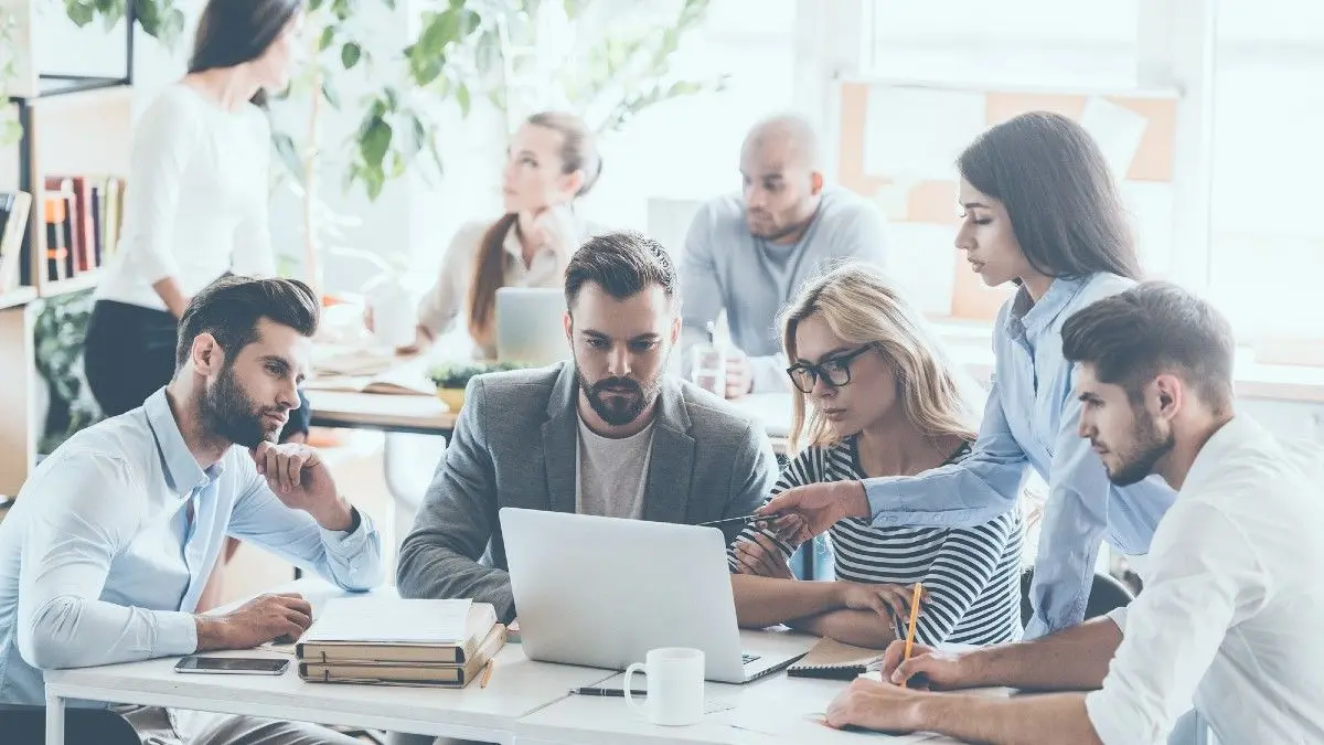 Group of business people working and communicating while sitting at the office desk together with colleagues sitting in the background