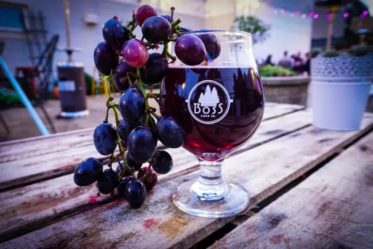 glass of cider on a wooden table surrounded by grapes