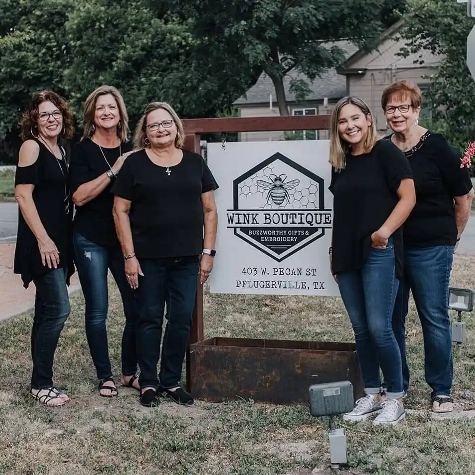 Wink Boutique team posing next to exterior sign  